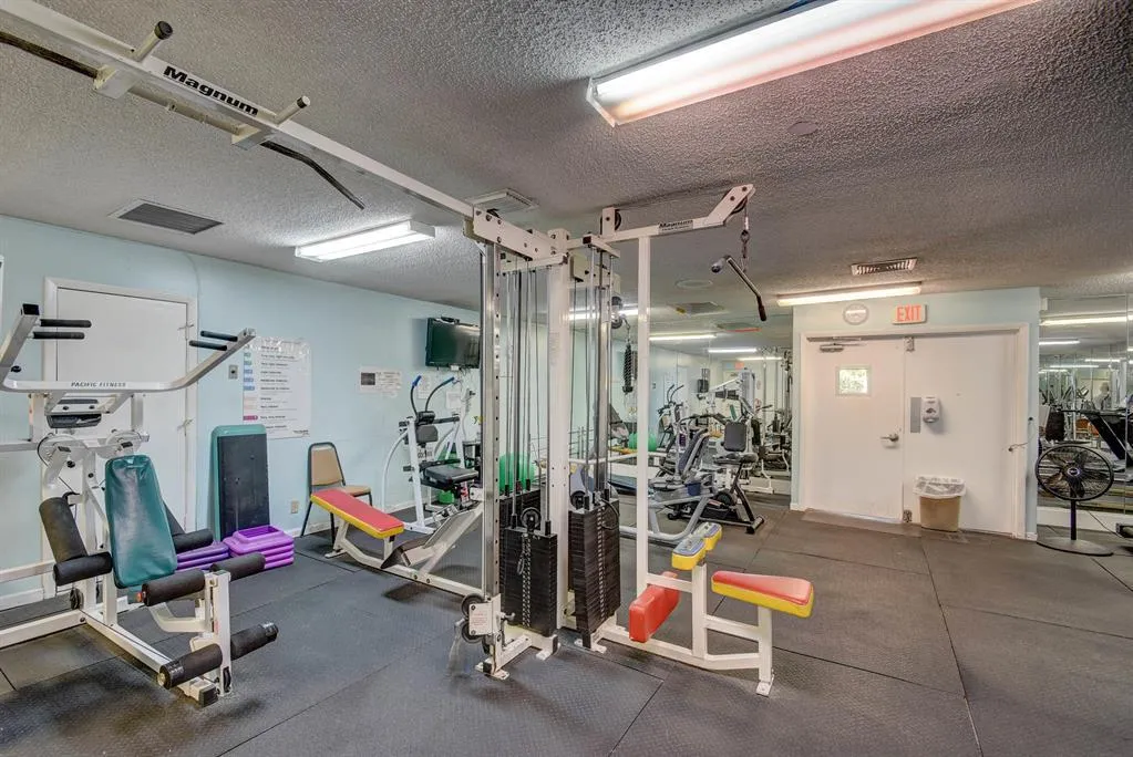 Dedicated fitness space featuring multiple exercise machines, mirrored wall, and durable rubber flooring