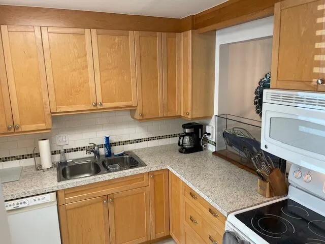Wood-finish cabinetry, white subway tile backsplash, stainless steel double basin sink, light-toned countertop, and built-in microwave