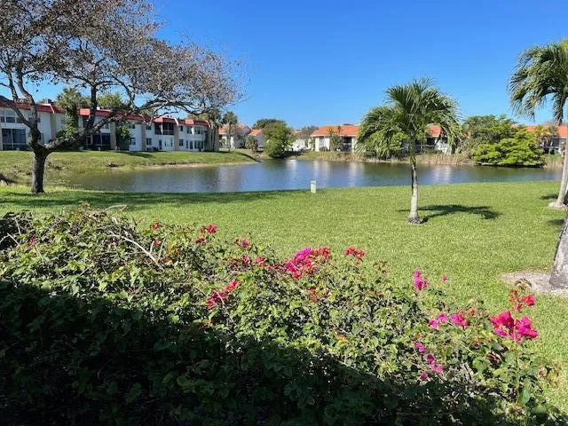 Expansive green space featuring a large body of water, mature trees, and vibrant flowering bushes