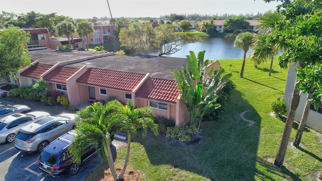Mediterranean-style architecture with red tile roofing, expansive green lawn, mature tropical landscaping, and a water feature