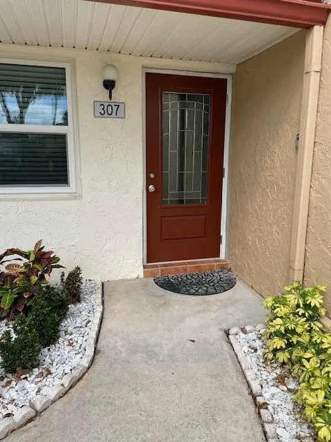 Red-toned front door with decorative glass inserts, exterior wall sconce, and white window trim