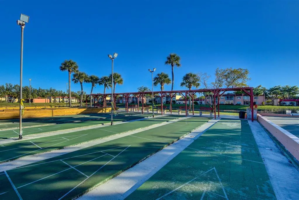 Shuffleboard courts with multiple lanes, illuminated by integrated floodlights, featuring a red pergola structure with bench seating