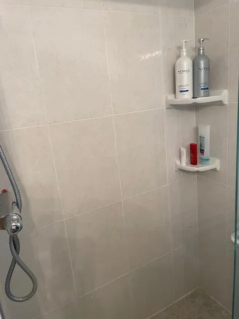 Tiled shower enclosure featuring light-toned square tiles and a glass panel