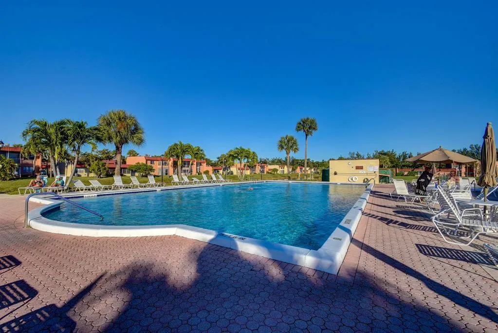 Expansive swimming pool with integrated spa, surrounded by a red paver deck and tropical landscaping
