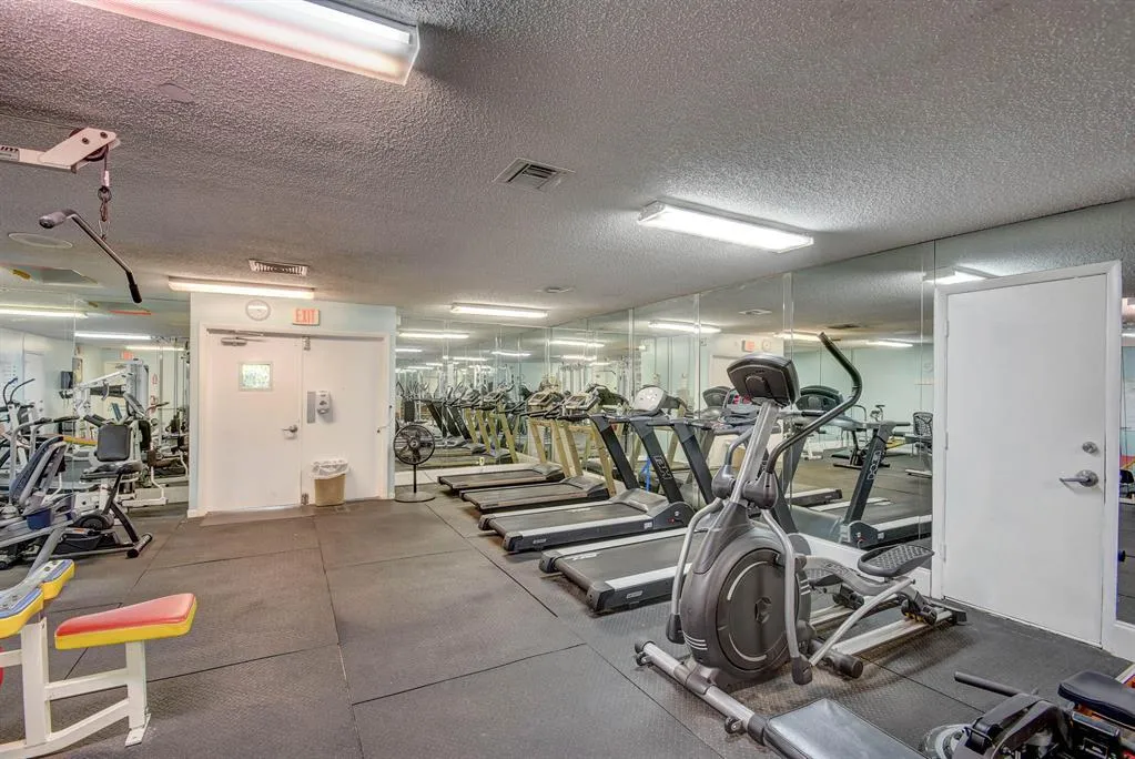 Fitness center featuring mirrored walls, resilient rubber flooring, overhead fluorescent lighting, and a selection of exercise equipment