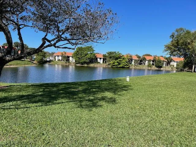Lush green lawn with a large body of water, bordered by residences with terracotta-style roofs and surrounding foliage