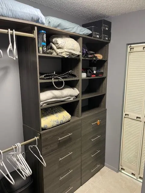 Custom closet system featuring a wood-finish, multi-drawer dresser unit with brushed nickel pulls, open shelving, and integrated hanging rods