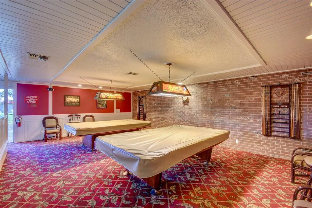 Recreation room featuring exposed brick walls, patterned carpet flooring, and dual suspended light fixtures