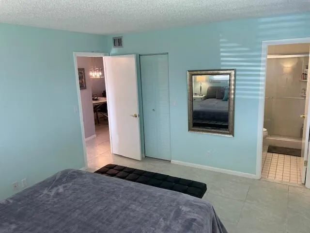 Light blue wall color, tile flooring, mirrored wall accent, built-in closet with bifold doors, and a bathroom entry with shower stall