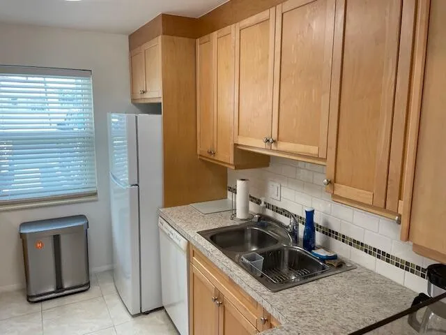 Kitchen featuring natural wood-finish cabinetry, white subway tile backsplash with decorative accent, laminate countertops, and tile flooring