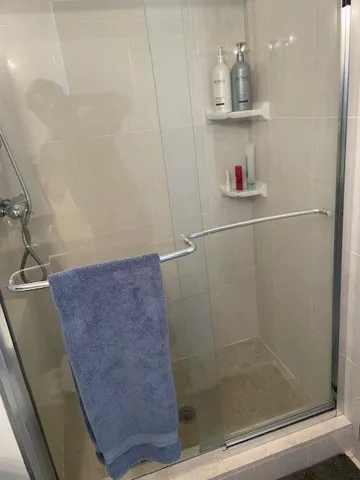 Glass-enclosed shower with a chrome showerhead, light-colored wall tiling, and built-in corner shelving