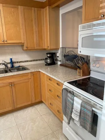 Full kitchen featuring light wood cabinetry, stone-finish countertops, tile backsplash, and a built-in microwave