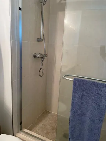 Shower enclosure with tiled walls, natural stone-finish shower pan, and a handheld shower fixture