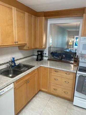 Recessed lighting, wood-finish cabinetry, stainless steel double basin sink, light-toned countertop, and white tile flooring