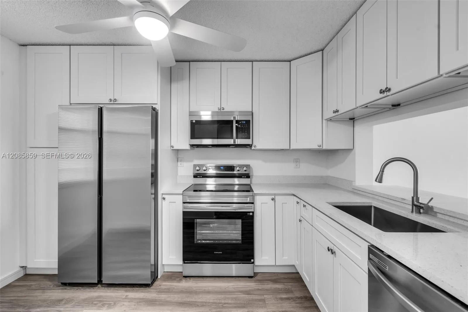 Updated kitchen equipped with clean white cabinetry, modern grey countertops, and sleek stainless steel appliances.