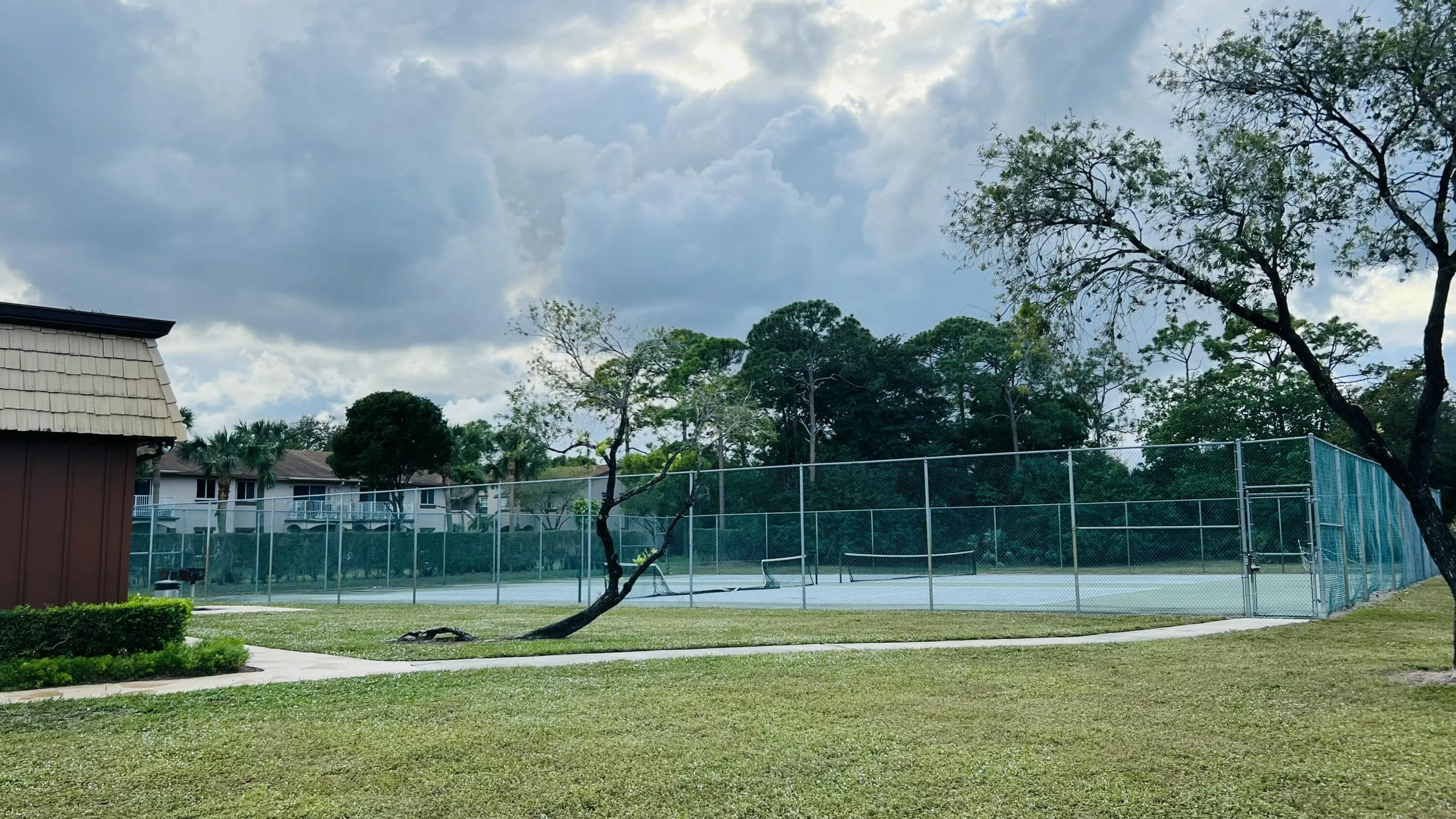 Recreational tennis court with chain-link fencing, surrounded by landscaped grounds and mature trees