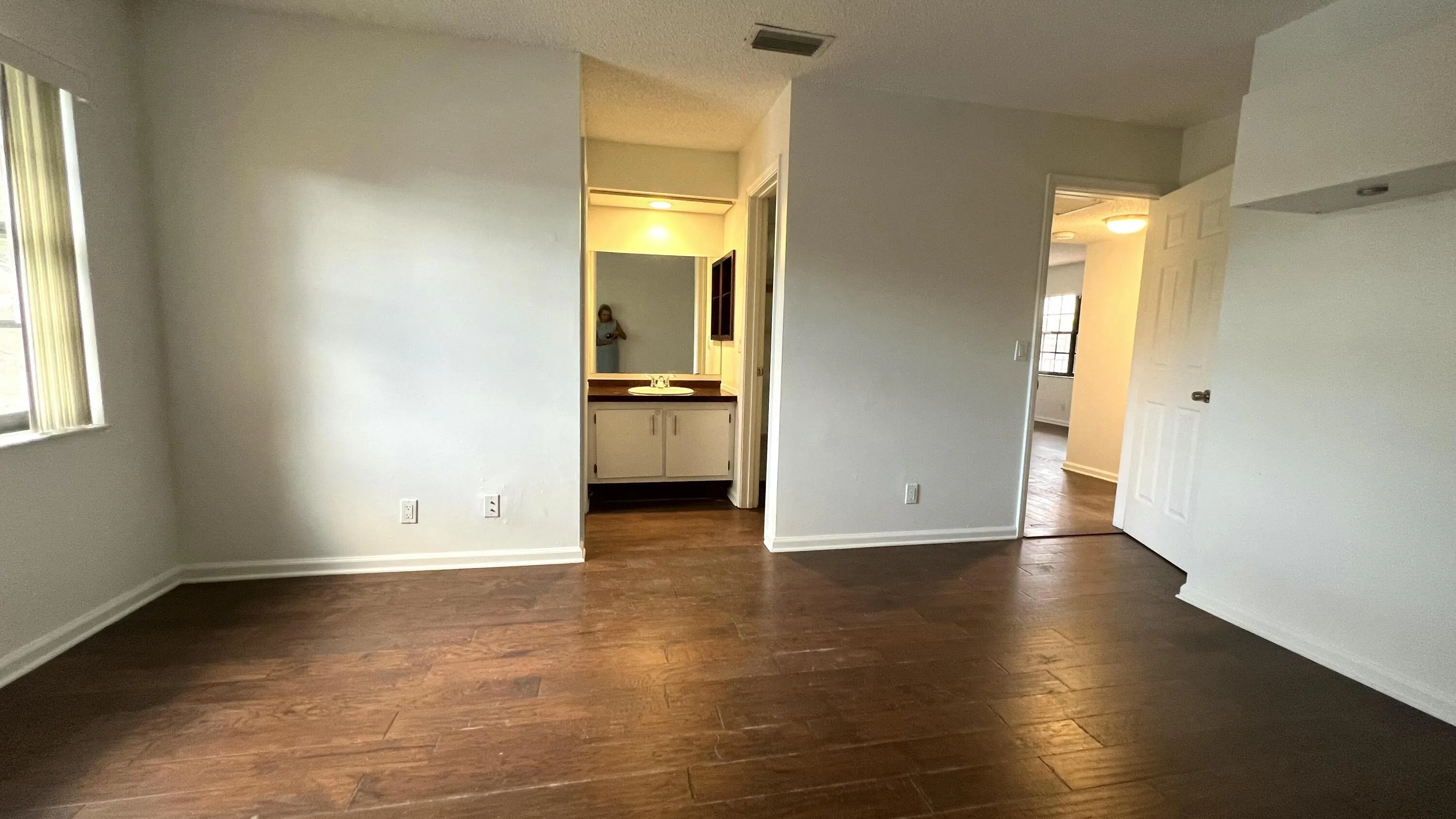 Wood-finish flooring, white walls, and a window with horizontal blinds