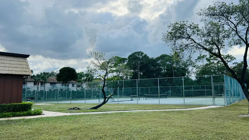 Recreational tennis court with chain-link fencing, surrounded by landscaped grounds and mature trees