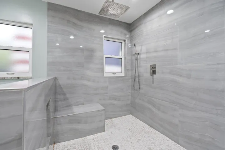 Walk-in shower with full wall tile, built-in bench, hexagon tile flooring, a rainfall showerhead, and a handheld shower attachment