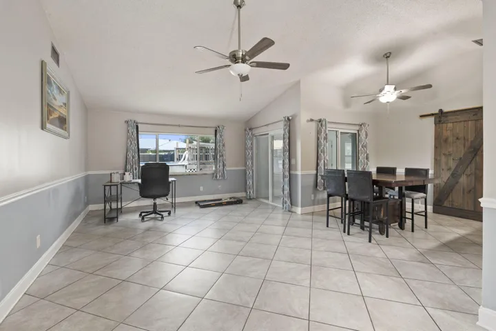 Spacious interior featuring tile flooring, vaulted ceilings, two ceiling fans with integrated lighting, and a sliding barn door