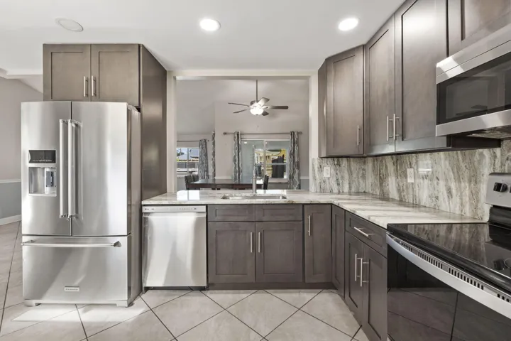 Contemporary kitchen featuring stainless steel appliances, dark wood-finish cabinetry, light stone countertops, and a matching stone backsplash