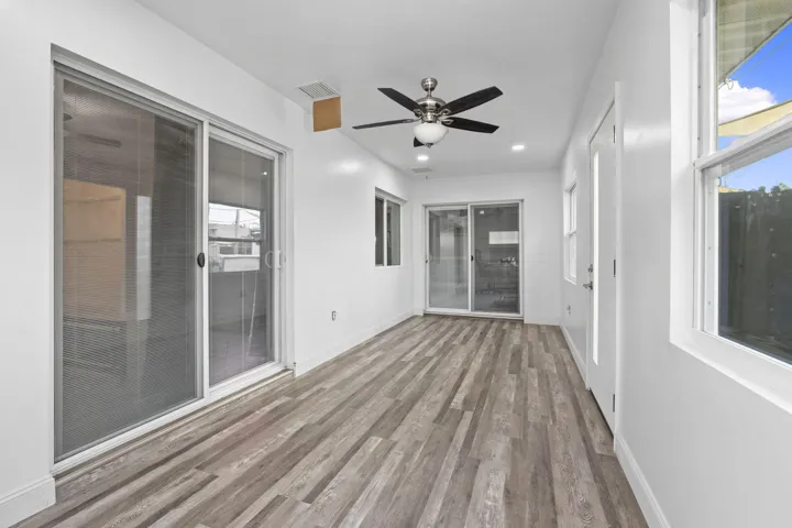 Bright interior space featuring wood-finish flooring, multiple sliding glass doors, white walls, and a ceiling fan