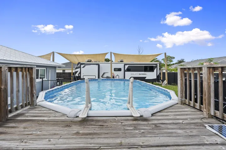 Expansive wood-finish deck with an above-ground pool, complemented by a metal roof structure and shade sails