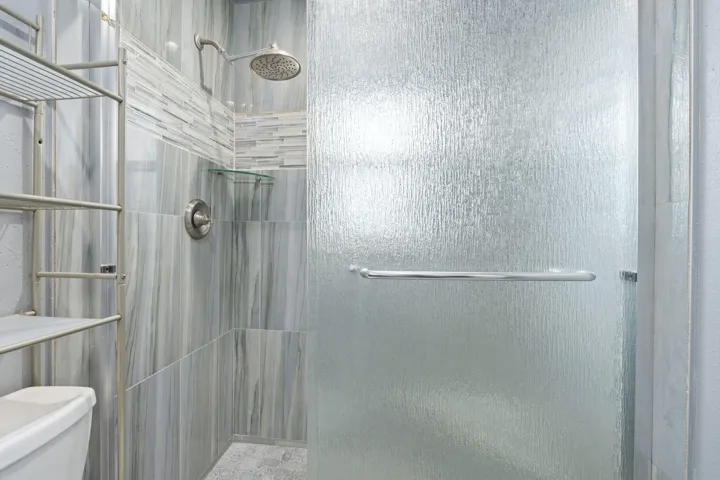 Walk-in shower with textured glass door, rain shower head, and tiled walls