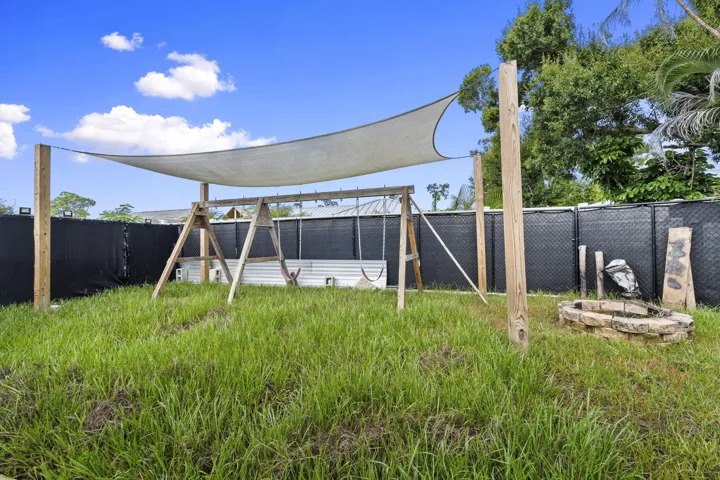 Shaded outdoor area featuring a swing set, sun shade sail, and a stone-built fire pit