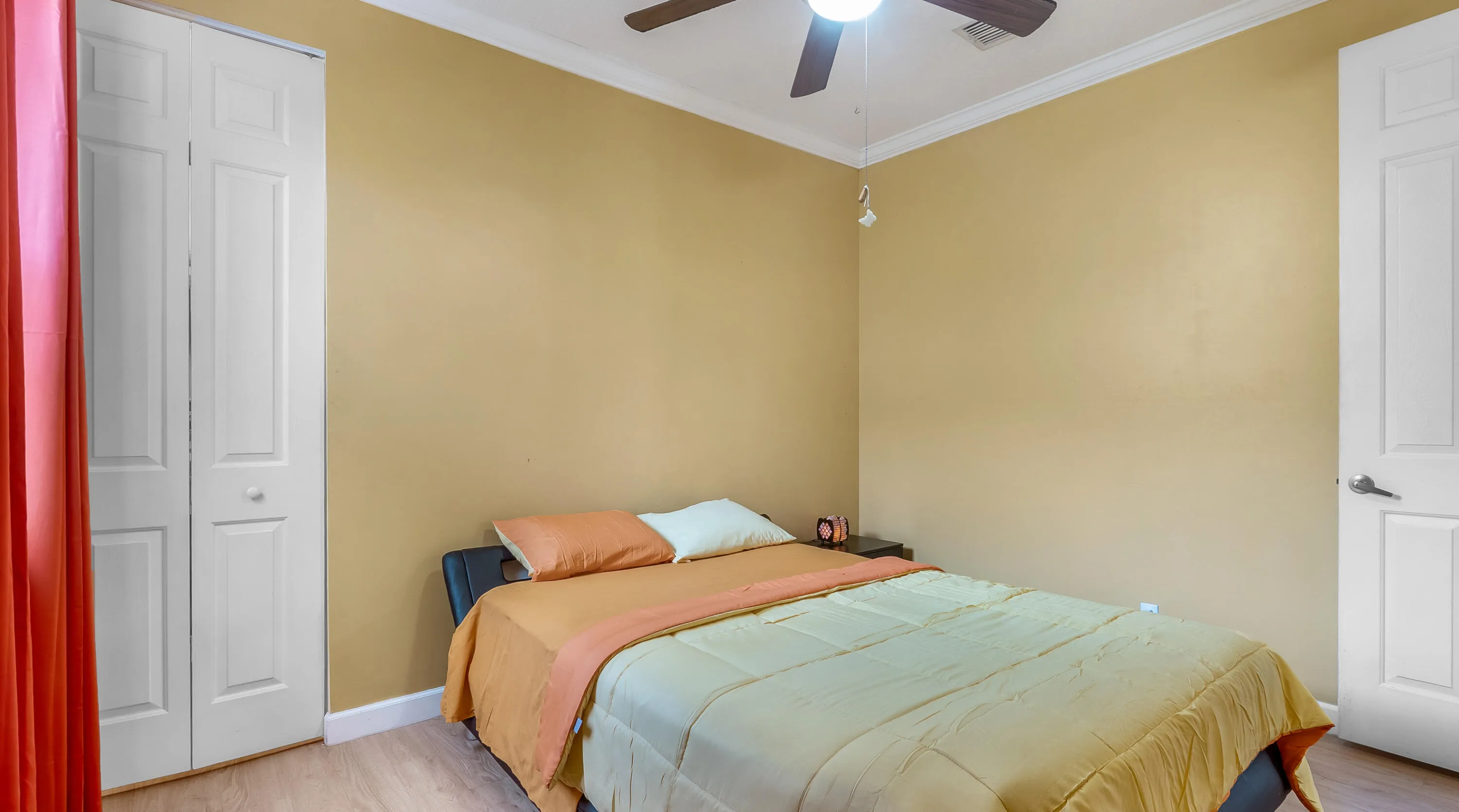Wood-finish flooring, white bi-fold closet doors, white panel door, crown molding, and a ceiling fan