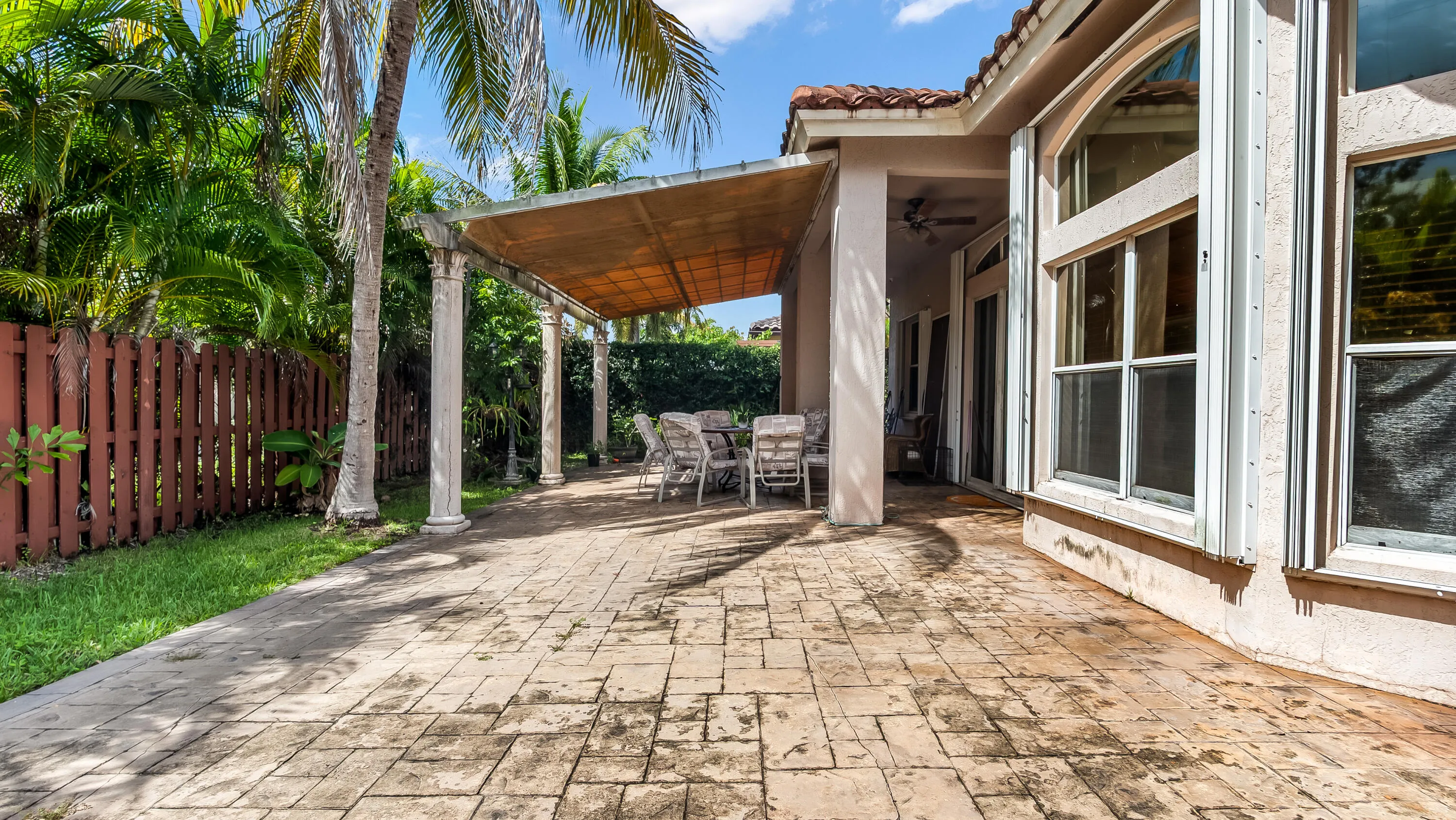 Expansive patio featuring a stone paver surface, pergola with fabric shade, privacy fence, and tropical landscaping