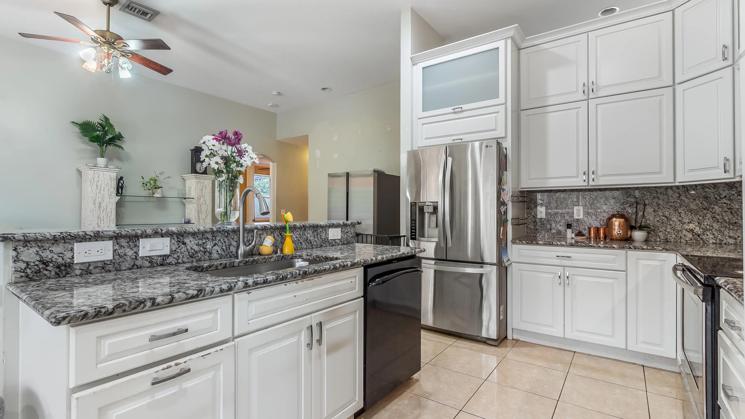 White cabinetry with brushed nickel hardware, speckled countertops, stainless steel appliances, and a tiled floor