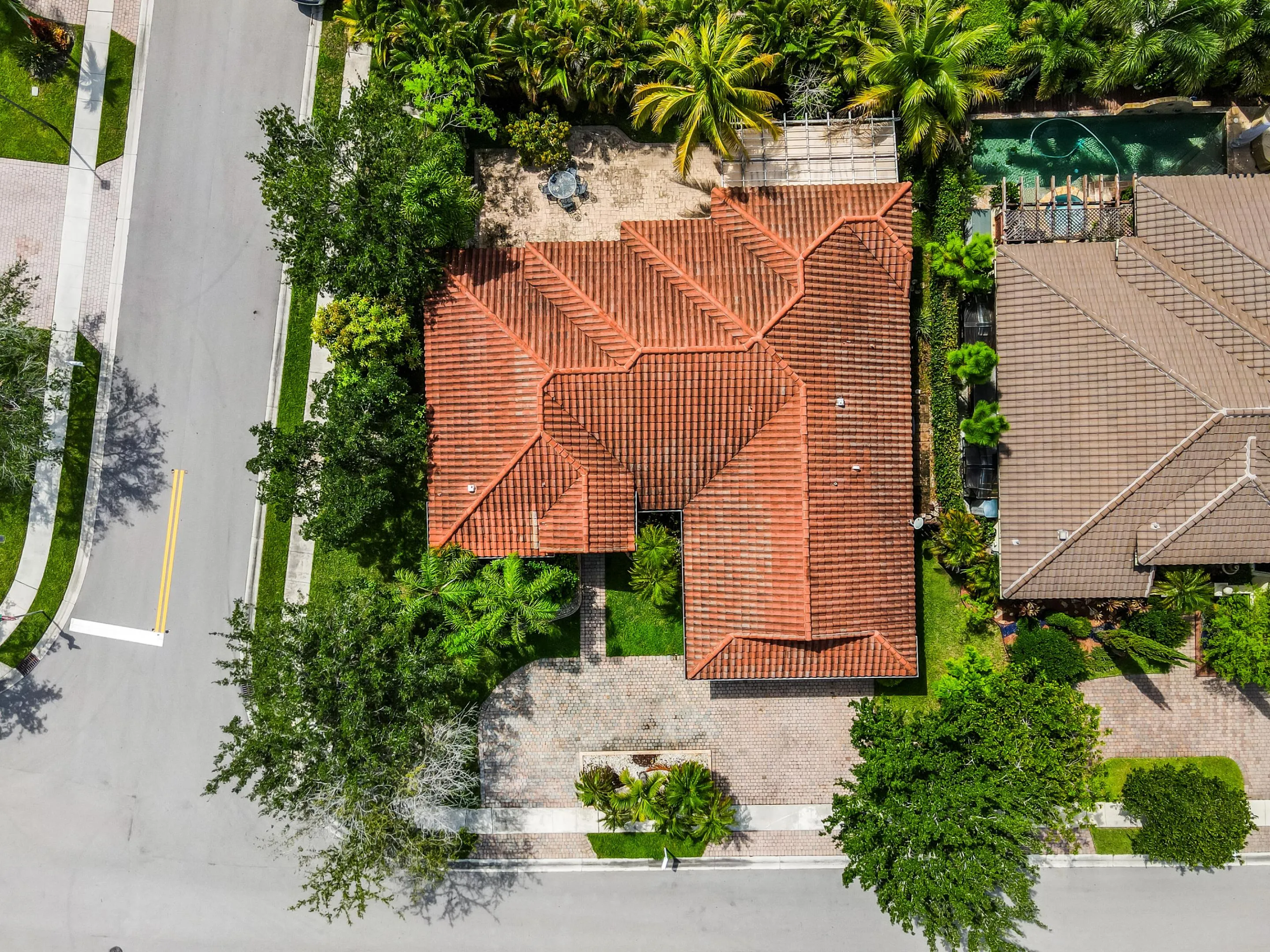 Red tile roof, mature landscaping, paved driveway, curving street frontage, and a lush green lawn