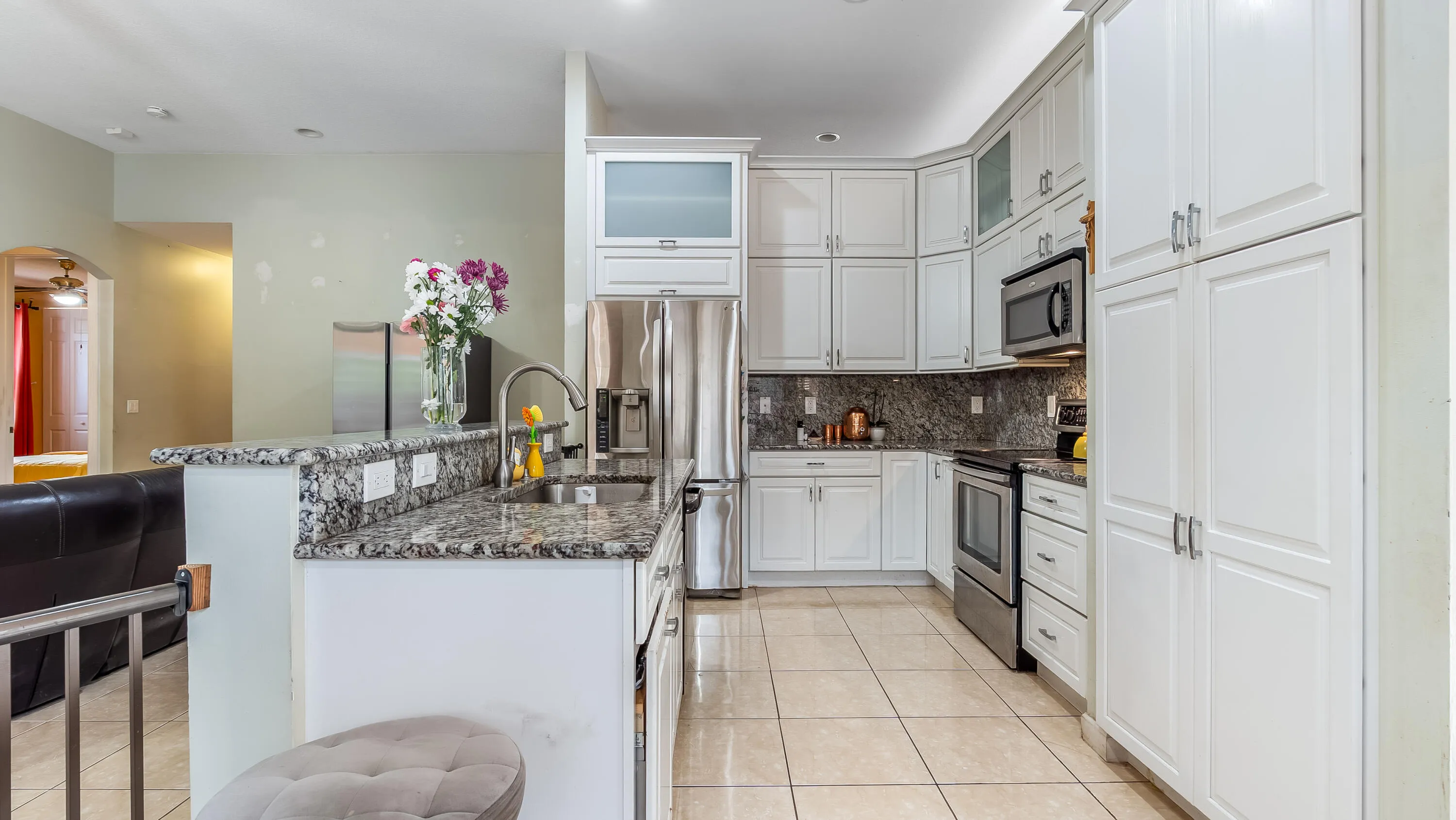 Kitchen featuring white cabinetry, granite countertops, stainless steel appliances, a stainless steel sink with a gooseneck faucet, and tile flooring