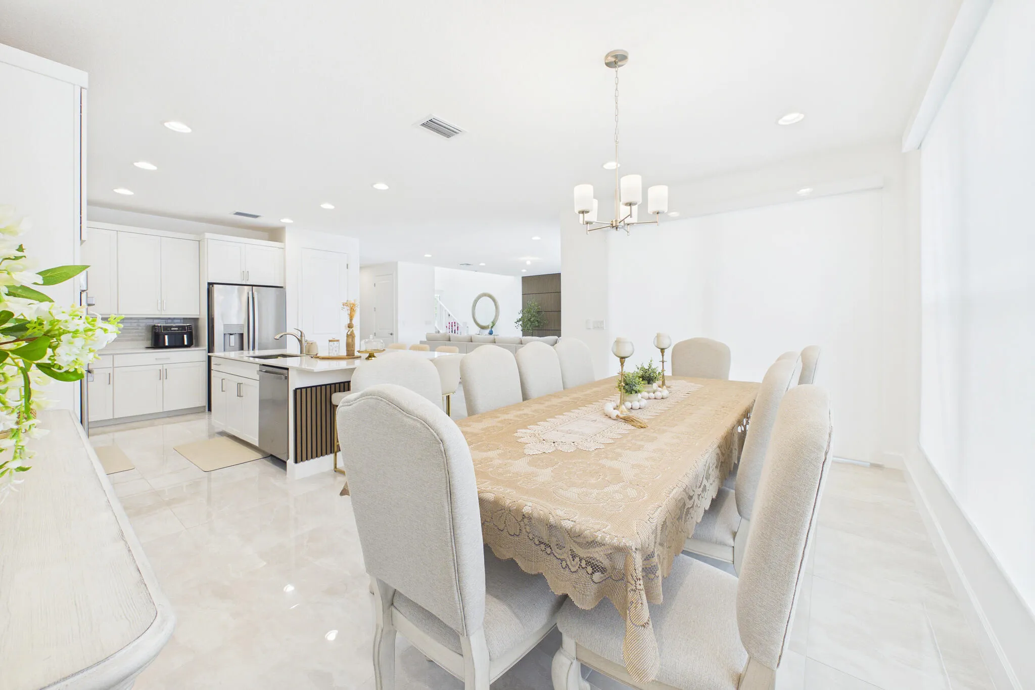 Open-concept living area with polished tile flooring, recessed lighting, a modern kitchen island with a sink, stainless steel appliances, and a contemporary chandelier