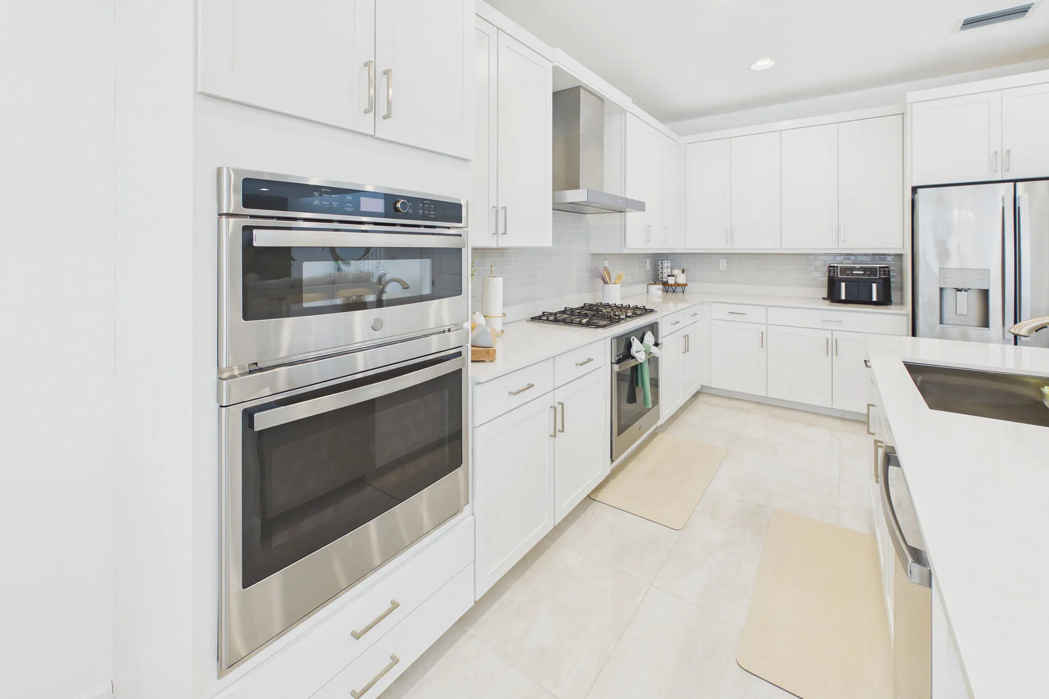 White cabinetry with brushed nickel hardware, stainless steel built-in double oven, stainless steel gas range with coordinating hood, and a stainless steel French door refrigerator