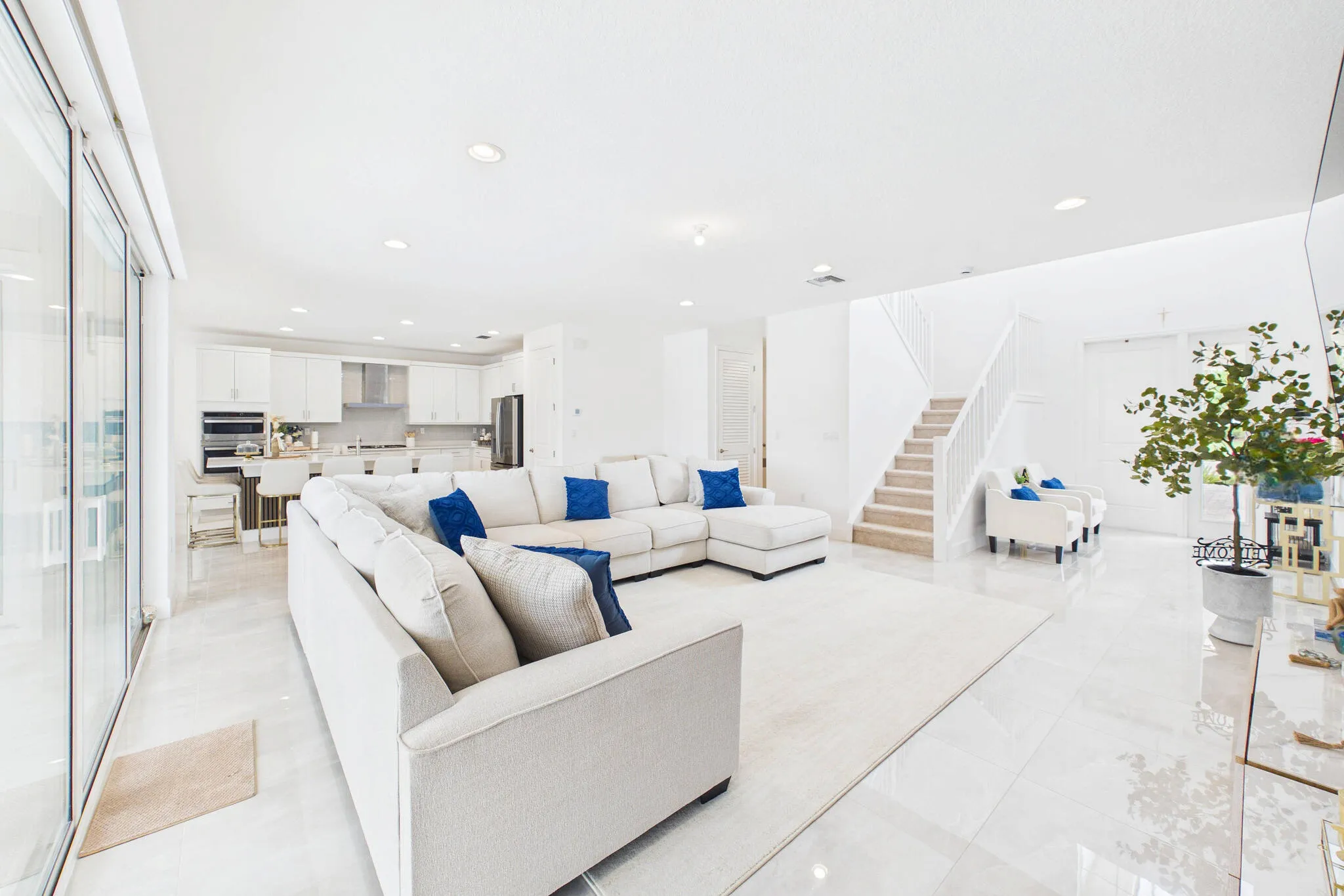 Open concept living space with white tile flooring, recessed lighting, and a white staircase with a carpet runner