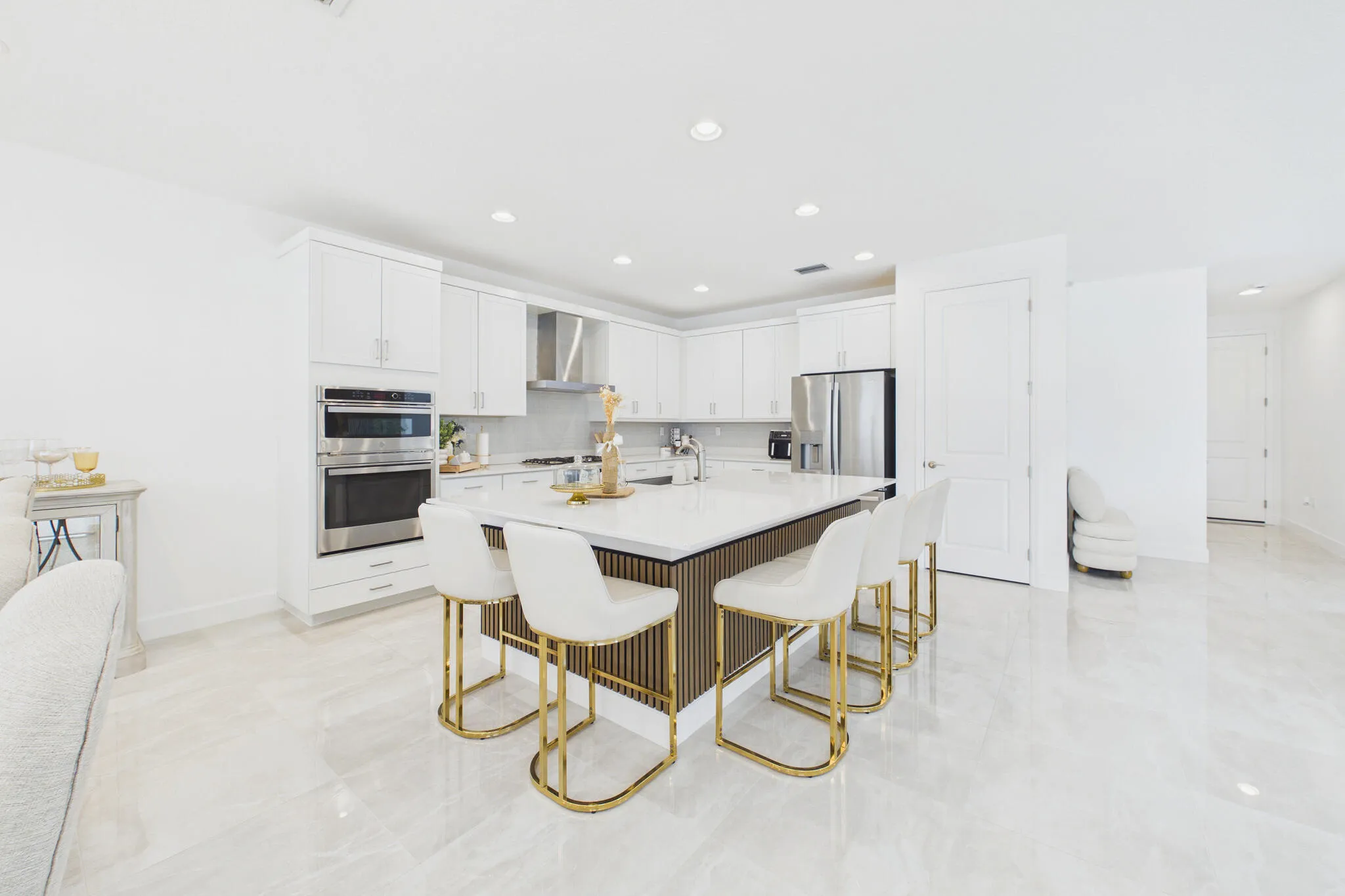 White kitchen cabinetry with stainless steel appliances, a center island with countertop seating, recessed lighting, and polished tile flooring