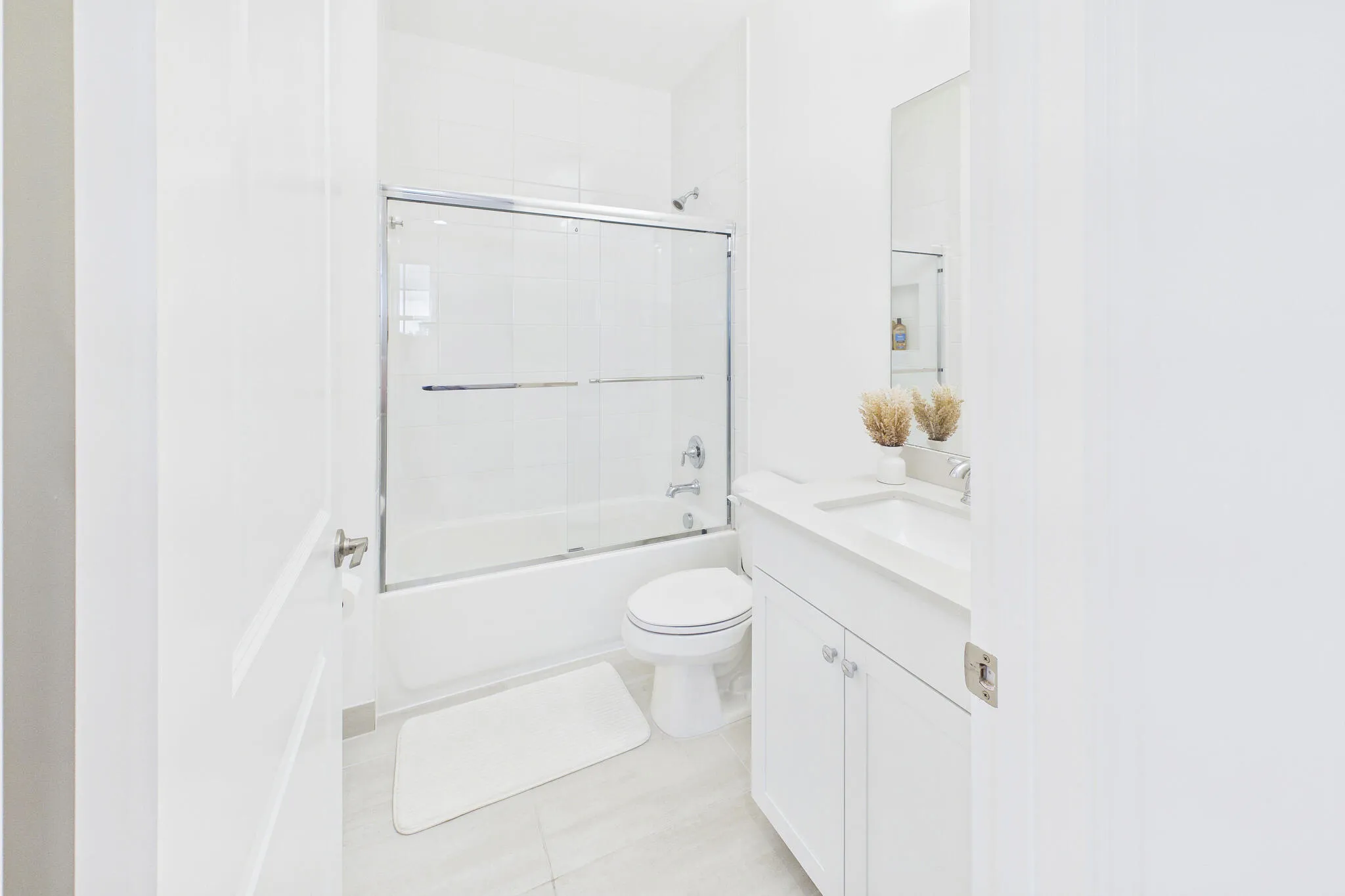 White porcelain bathtub with a sliding glass shower door, integrated single-sink vanity, and a wall-mounted mirror
