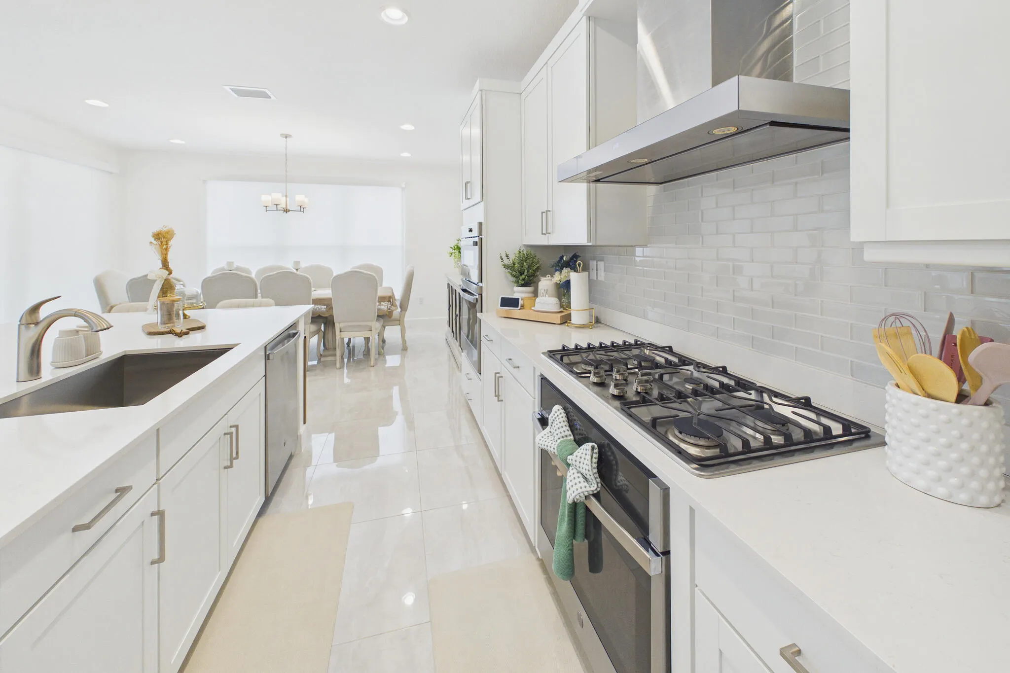 Kitchen with white cabinetry, stainless steel appliances, a gas range with a range hood, a kitchen island with an undermount sink, and tiled flooring