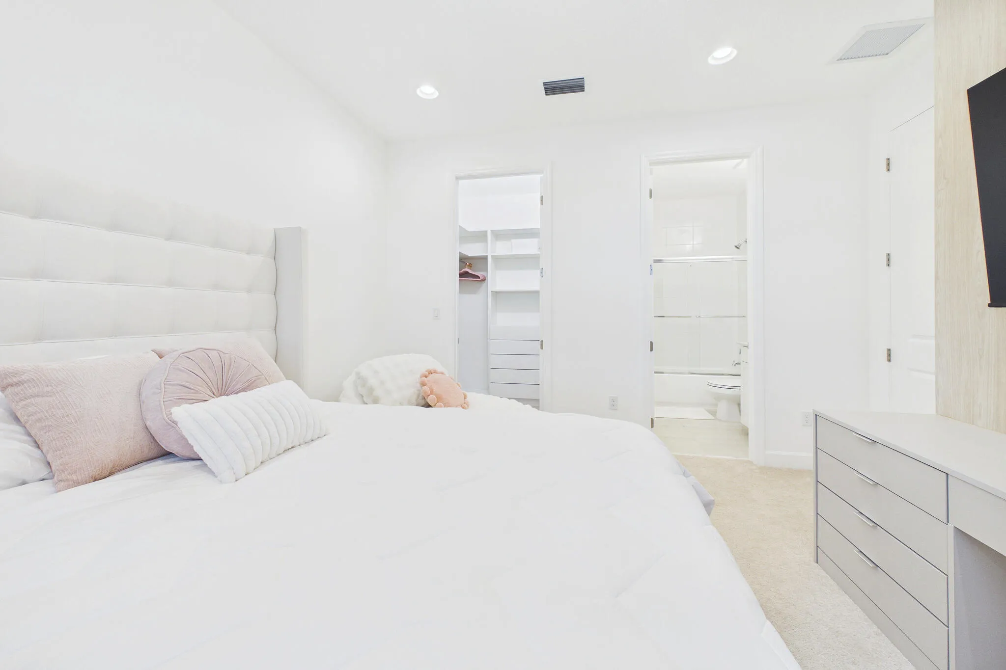 Recessed lighting, light-toned carpeting, built-in shelving, and a clean white bathroom with a shower-tub combination