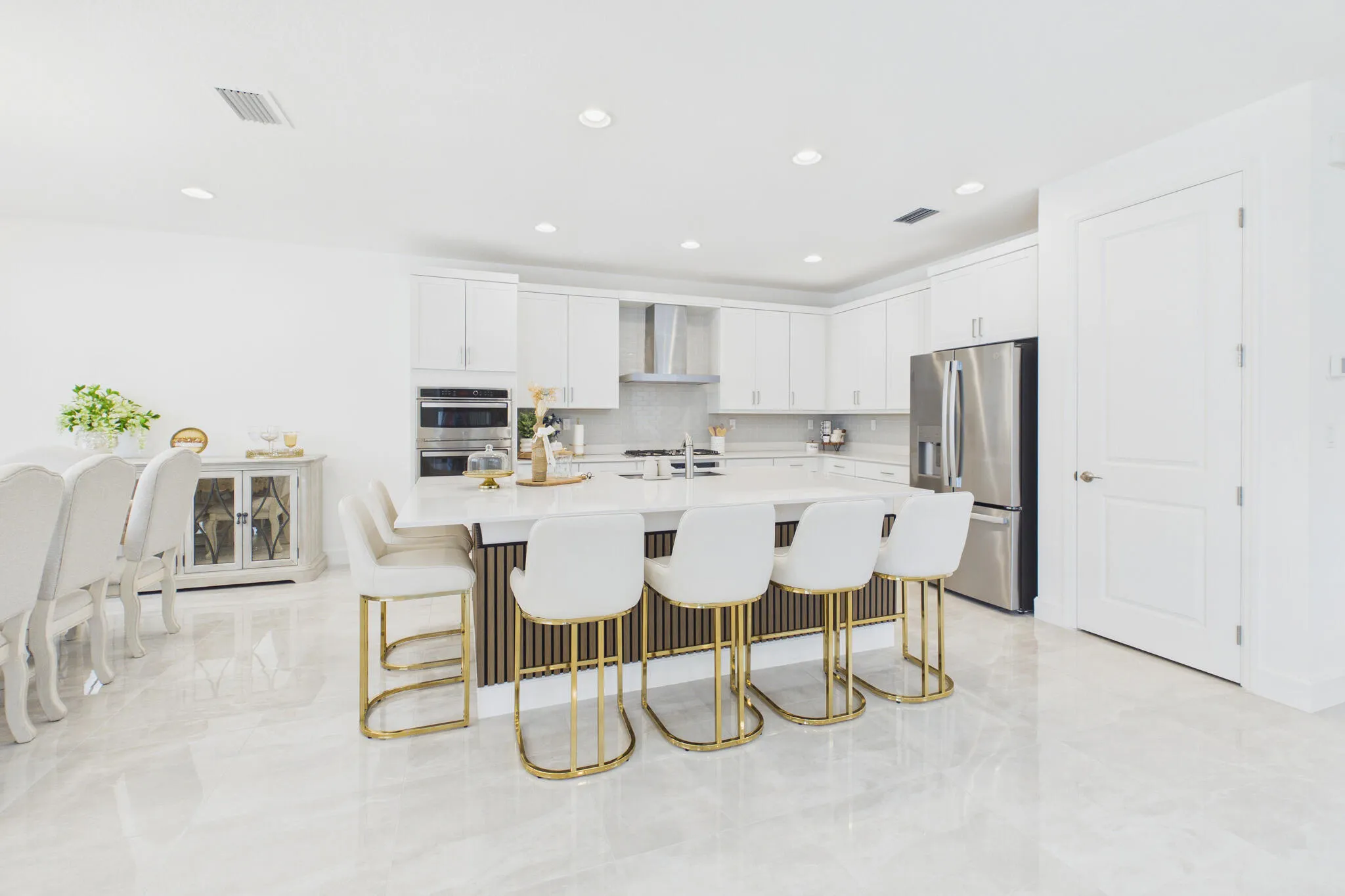 Open-concept kitchen with a large central island, white cabinetry, integrated double wall ovens, stainless steel refrigerator, and light-toned tile flooring