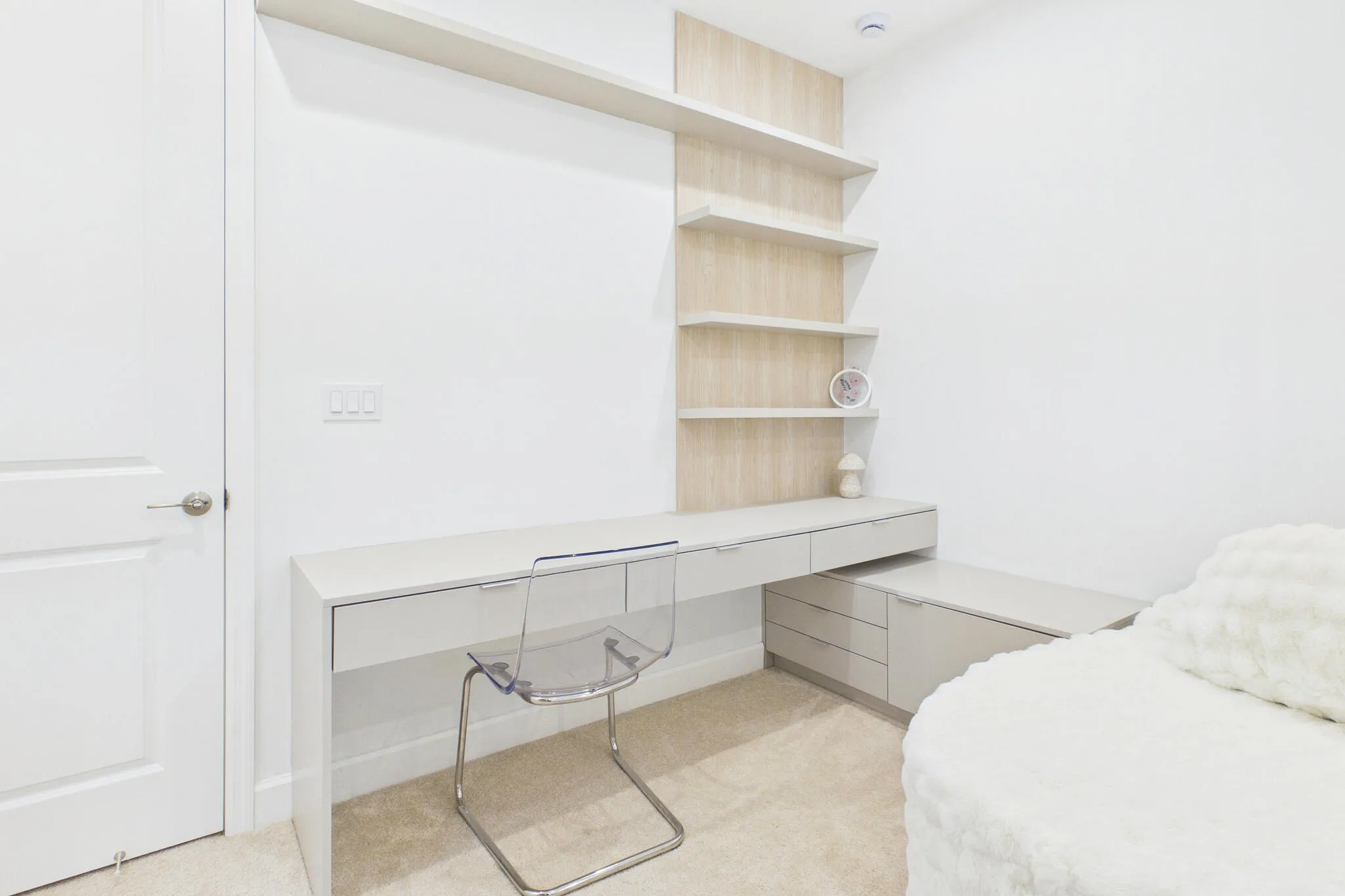 Built-in desk with integrated drawers, neutral carpet flooring, and custom shelving with wood-finish backing