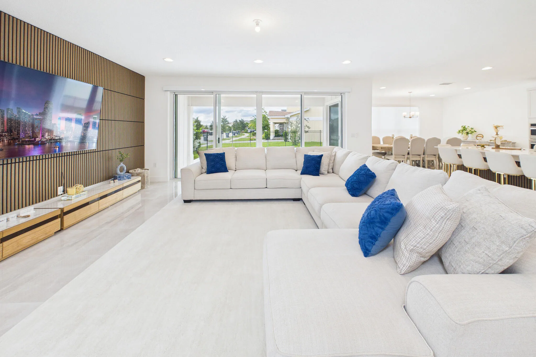 Spacious living area featuring light-toned flooring, recessed lighting, a slatted wood-finish accent wall, and sliding glass doors