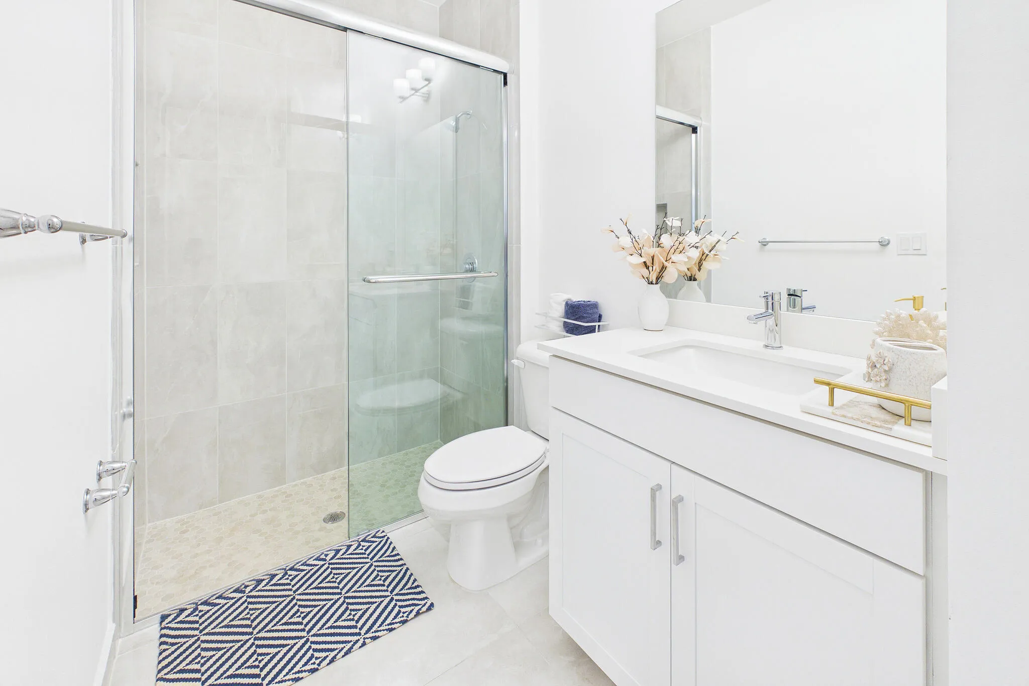 White vanity with integrated sink and chrome faucet, glass-enclosed shower with subway tile surround, recessed lighting, and a wall-mounted mirror