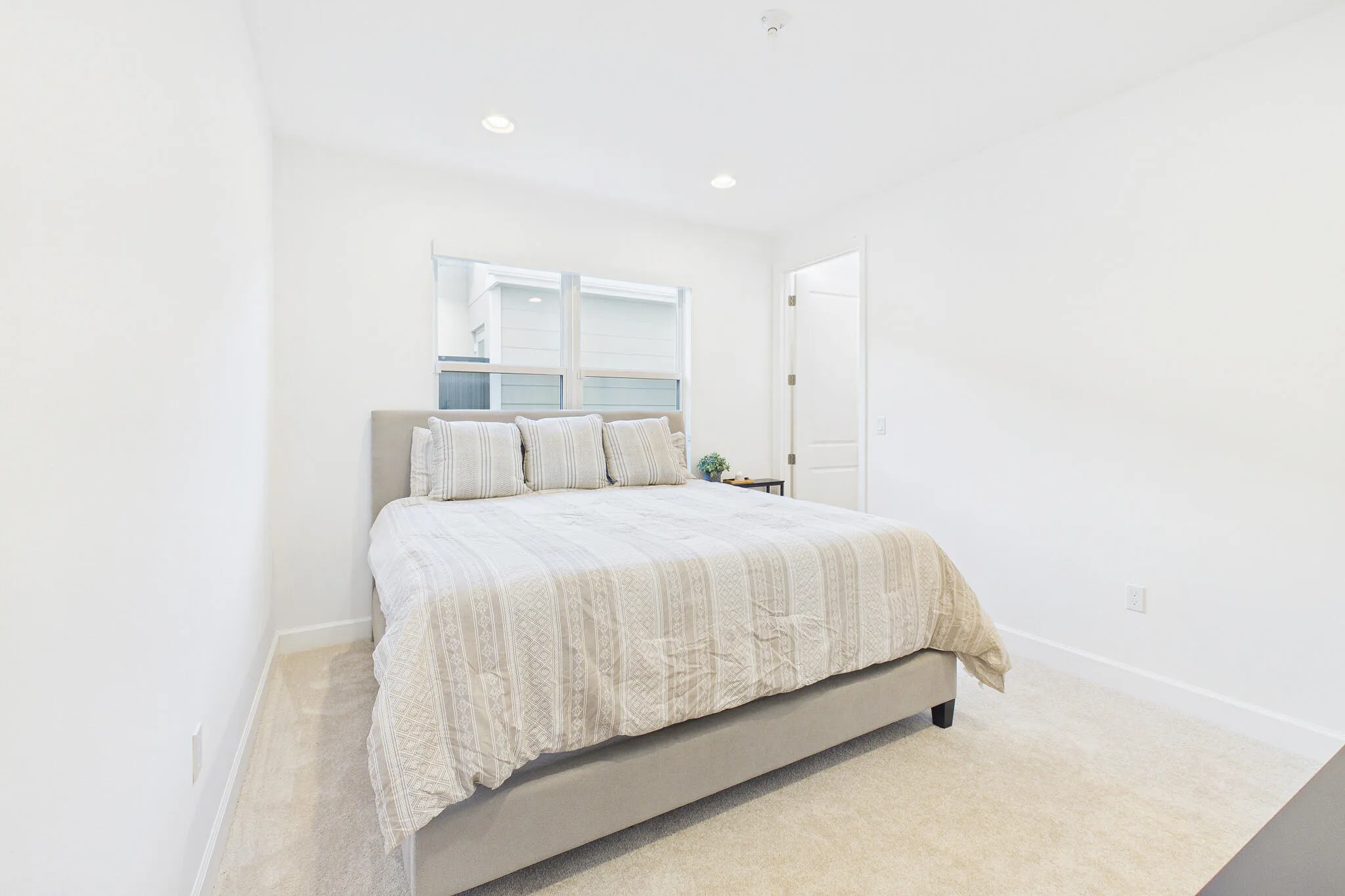 Recessed lighting, light-colored carpeting, white interior walls, and a window with white trim
