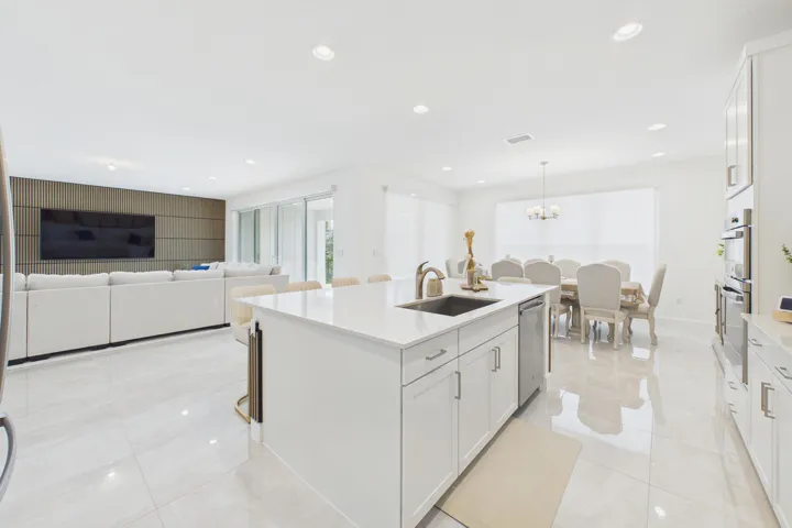 Open-concept living area featuring a kitchen island with sink and stainless steel dishwasher, an adjacent dining space with chandelier, and a living area with a decorative wood-panel accent wall