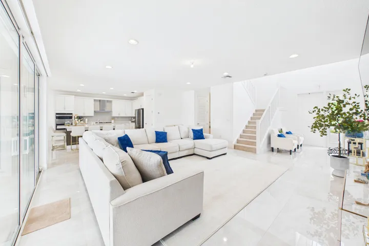 Open concept living space with white tile flooring, recessed lighting, and a white staircase with a carpet runner