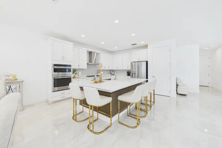 White kitchen cabinetry with stainless steel appliances, a center island with countertop seating, recessed lighting, and polished tile flooring