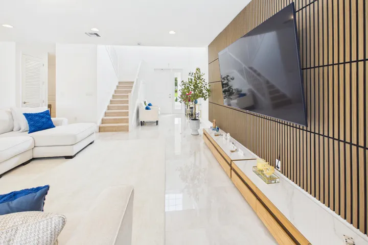 Sleek wood-slat accent wall with integrated media console, polished tile flooring, recessed lighting, and a staircase with open risers